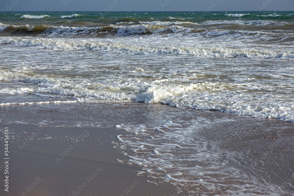 A sea wave runs onto the sand of a beach with foam on shore. Seascape in sunset colors. Beautiful natural background for design and decoration