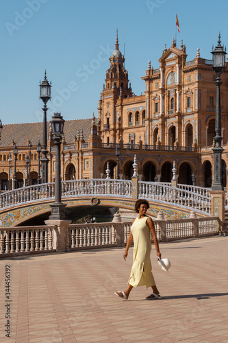 afro american woman in plaza españa, sevilla. girl wearing a yellow dress and white hat