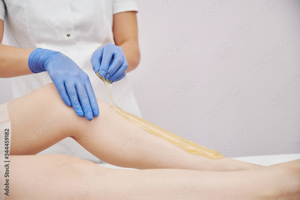 Fototapeta premium the procedure shugaring. master in blue medical gloves apply sugar paste with his hands