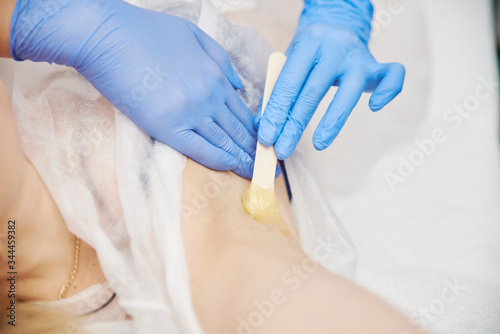 the procedure shugaring. master in blue medical gloves apply sugar paste to the client's armpit