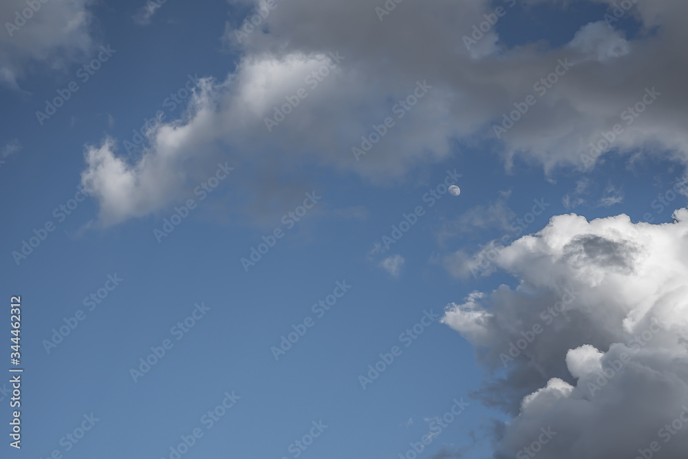 Obraz premium Blue sky with white clouds. Moon among clouds against a blue sky.