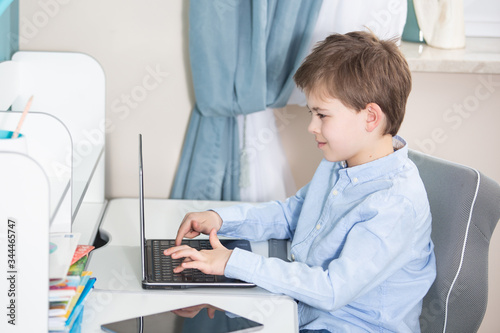 work from home - smiling young boy in blue shirt sits at his desk working on his notebook computer