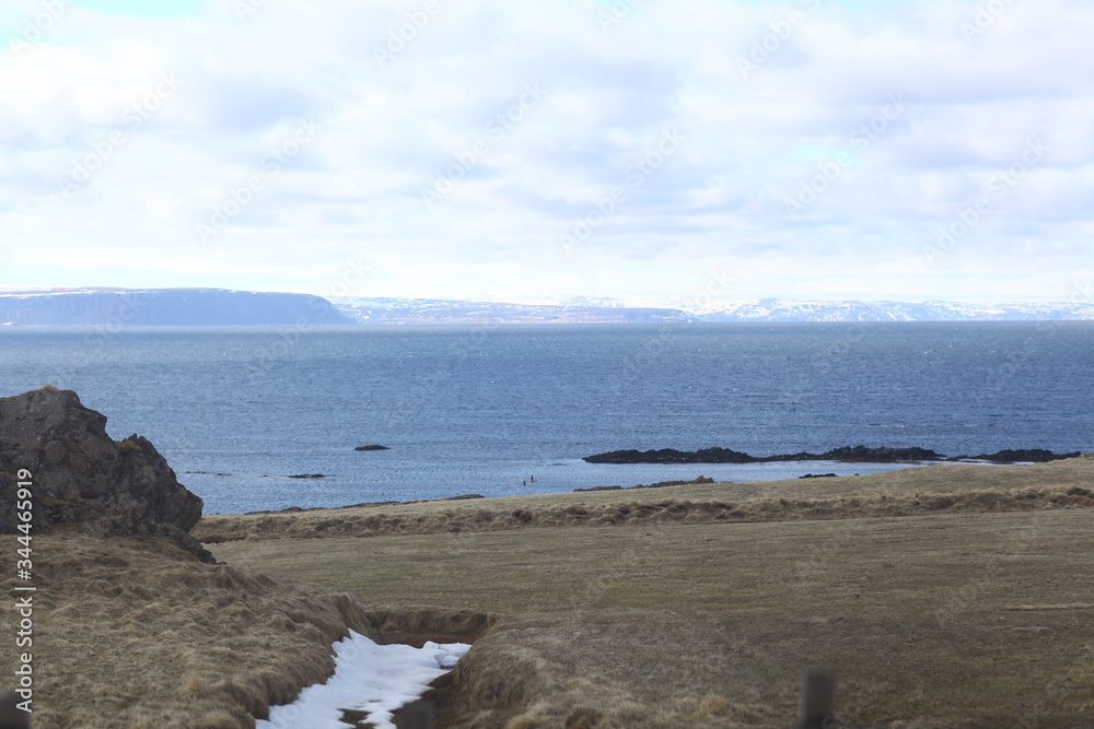 White snow on the mountains in the distance, beautiful blue ocean and the yellow grass in the foreground