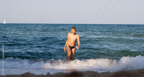 A teenager comes out of the sea to the beach.