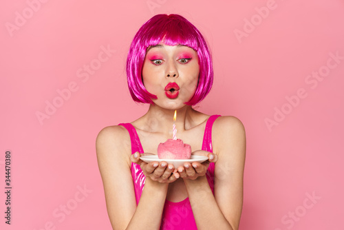 Image of young beautiful woman in wig blowing out candle on cake