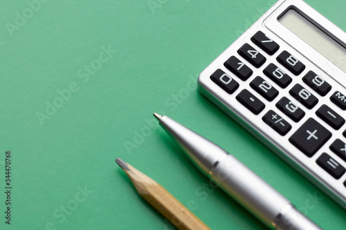 Close-up of a calculator, pen and pencil on a green background in the top view. Concept of educational activities