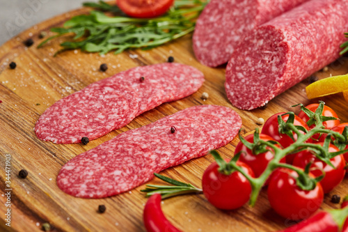 Traditional thinly sliced salami on a wooden cuttingboard with spices, lettuce, avocado and tomatoes. Cold meat plate