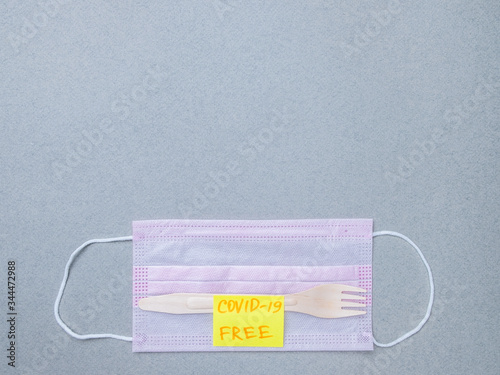 Wooden fork, pink medical mask and sticker with the inscription covid-19 free on a gray background. The concept of delivering safe, uninfected food during the quarantine coronavirus. Layout copy space photo