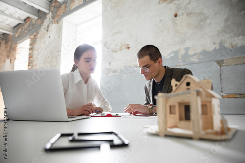 New solutions. Female estate agent showing new home to a young man after a discussion on house plans. Choosing construction materials, repair, technologies in smart house. Moving, new home concept.