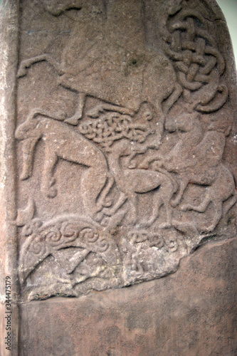 Ancient abstract design carved onto a standing stone in northern europe. Shows animals and riders on horses possibly hunting.
