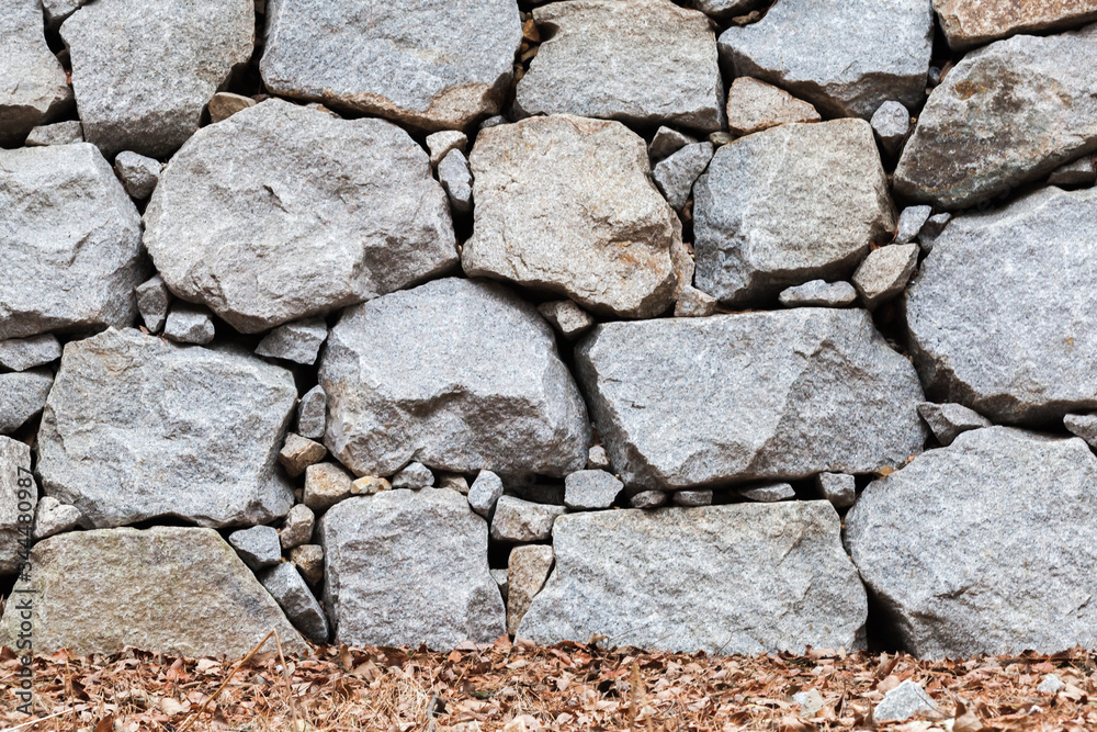 Obraz premium Old wall made of rough gray stones and dry leaves