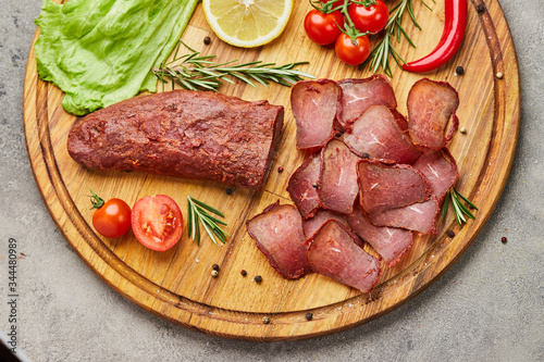 Armenian basturma or Pastirma on wooden cutting board decorated with spices, lettuce, lemon and tomatoes. Meat smoked jerky good as Beer snack
