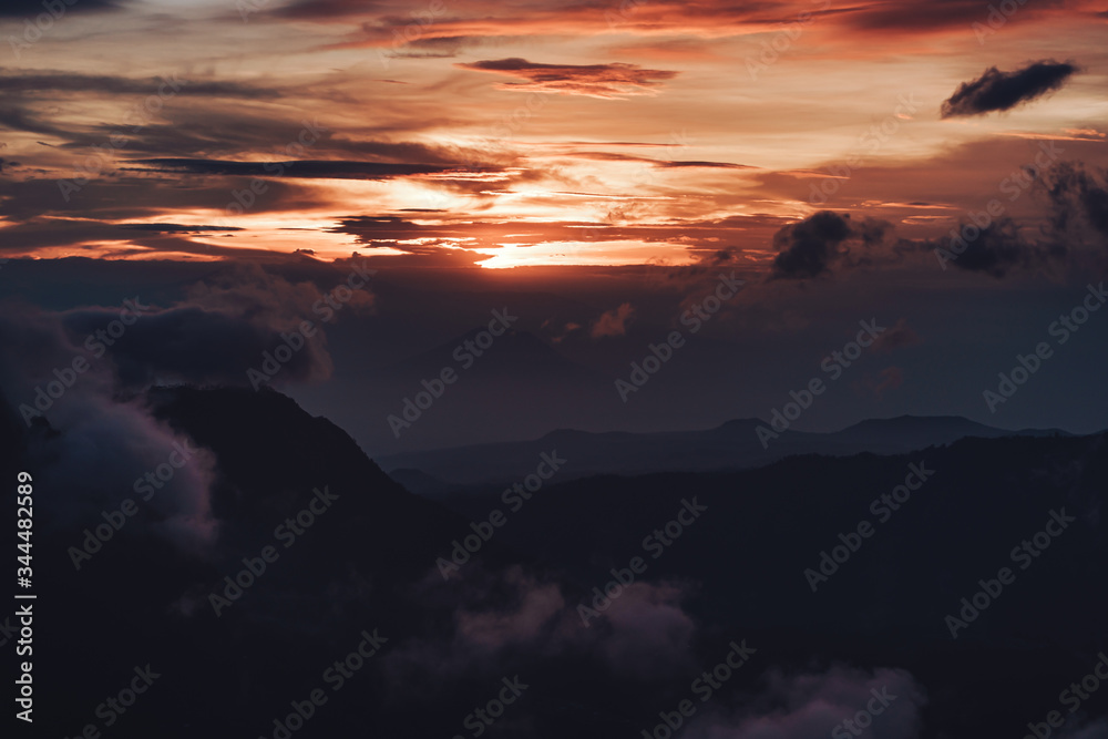 Dark photo of sunrise in mountains with clouds and sun rays on Java