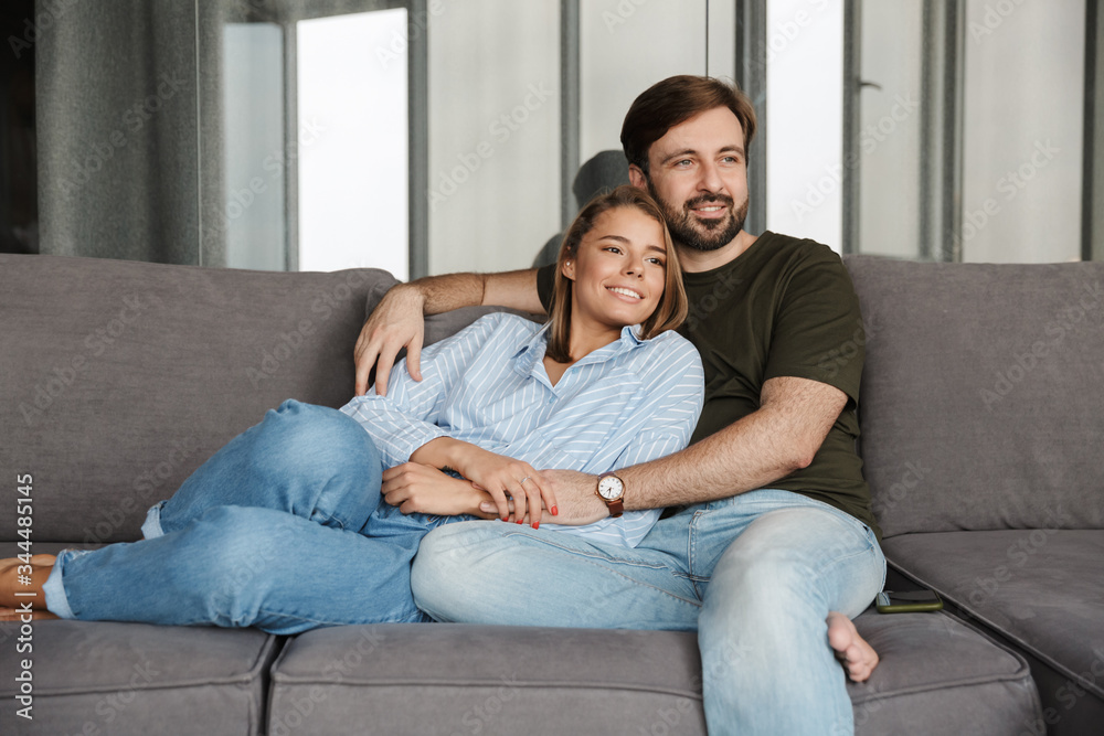 Photo of cheerful couple smiling and hugging while sitting on sofa Photo of cheerful couple smiling and hugging while sitting on sofa