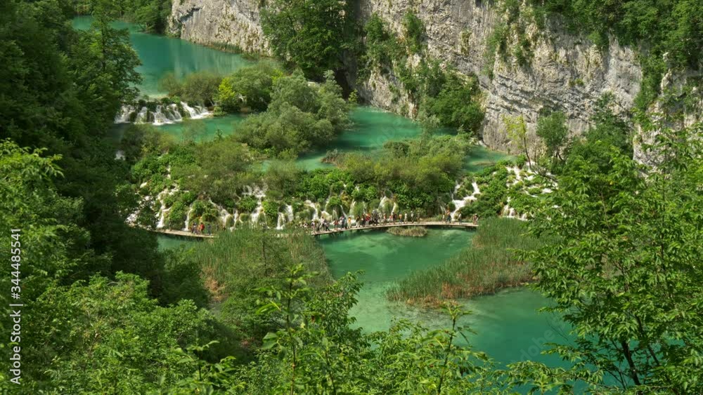 Plitvice Lakes National Park, Croatia. General view of a lake with many small cascades. Many tourists walking the boardwalk. Rich greens, UHD Plitvice Lakes National Park, Croatia. General view of a lake with many small cascades. Many tourists walking the boardwalk. Rich greens, UHD