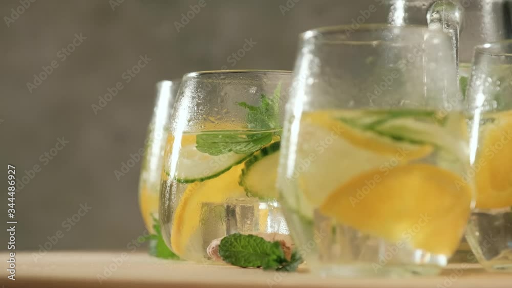 Rotating of glasses with summer healthy lemonade, cocktails of citrus infused water or mojitos, with lime lemon orange, ice and mint, diet detox beverages, on gray background. Rotating of glasses with summer healthy lemonade, cocktails of citrus infused water or mojitos, with lime lemon orange, ice and mint, diet detox beverages, on gray background.