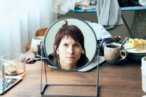 Tableau sur toile Woman looks at herself in mirror against background of mess, dirty dishes, piles