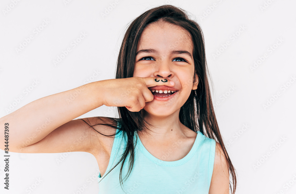 Indoor portrait of funny little girl grimacing and smiling broadly with mustache drawing on her index finger put it under the nose. Cute child having fun and playing on white background. Indoor portrait of funny little girl grimacing and smiling broadly with mustache drawing on her index finger put it under the nose. Cute child having fun and playing on white background.