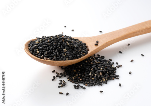 Black sesame seeds in a wooden spoon placed on a white background