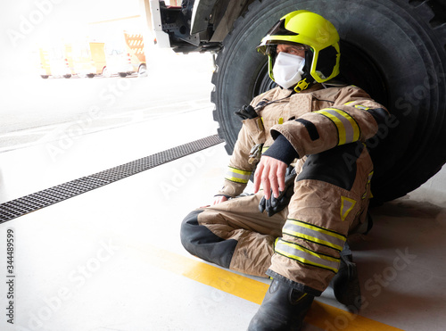 Firefighter sitting next to truck with mask and helmet to protect himself from the covid 19