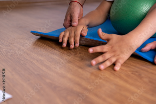 Little boy with cerebral palsy has musculoskeletal therapy by doing exercises on floor mat. Child give hand therapist