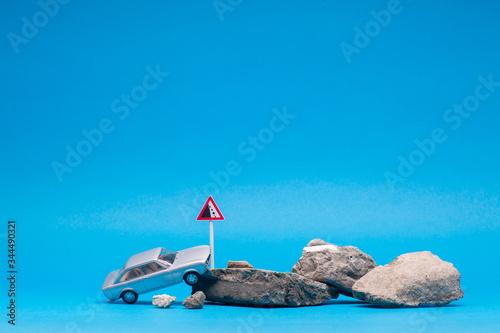 A light blue car next to a bunch of stones, on blue background.