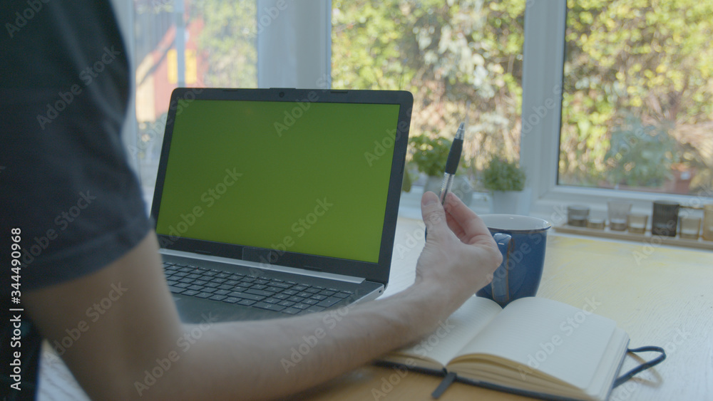 Working from home using a green screened laptop on the kitchen table with pens and a pad Working from home using a green screened laptop on the kitchen table with pens and a pad