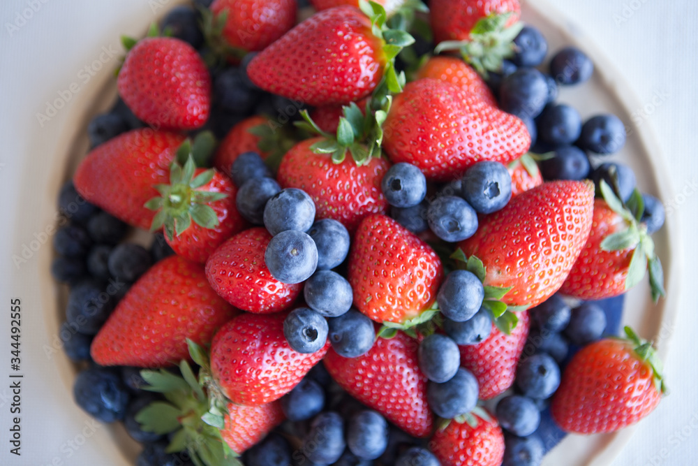 Blueberries and strawberries in a ceramic plate on the table. Natural light. Blueberries and strawberries in a ceramic plate on the table. Natural light.