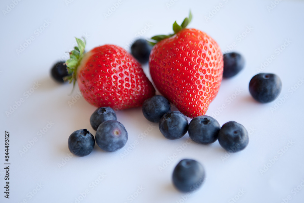 Ripe and juicy strawberries and blueberries scattered on the table. Neutral light. White background. Ripe and juicy strawberries and blueberries scattered on the table. Neutral light. White background.