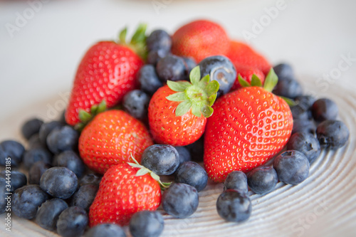 Blueberries and strawberries in a ceramic plate on the table. Natural light.