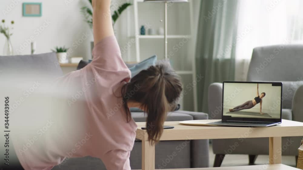 Young woman doing side plank exercise and then listening to fitness instructor while having online workout on laptop during quarantine at home Young woman doing side plank exercise and then listening to fitness instructor while having online workout on laptop during quarantine at home