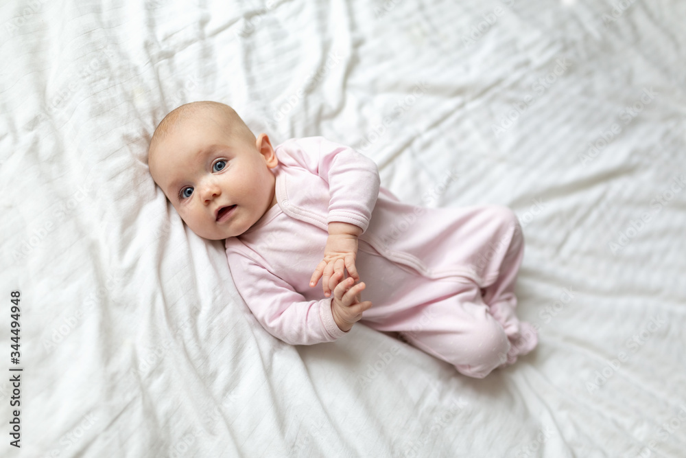 A cute little baby is smiling lying on the bed on a white sheet in the parents bedroom. Closeup portrait of newborn baby looking at camera A cute little baby is smiling lying on the bed on a white sheet in the parents bedroom. Closeup portrait of newborn baby looking at camera