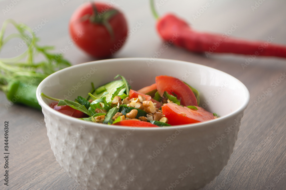 Healthy fresh summer salad with cucumbers, tomatoes, fresh arugula, chopped walnuts, pepper, olive oil and lemon juice on a rustic wooden surface Healthy fresh summer salad with cucumbers, tomatoes, fresh arugula, chopped walnuts, pepper, olive oil and lemon juice on a rustic wooden surface