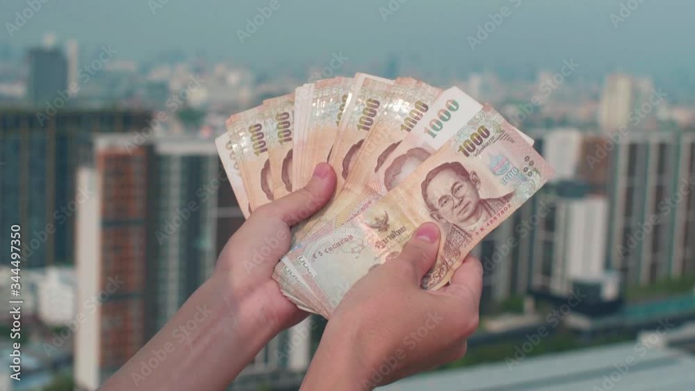 Thai baht bills - counting money on building's rooftop big city Bangkok cityscape