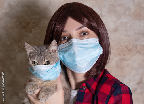 Woman in protective surgical mask holds grey cat pet in face mask. Chinese Coronavirus disease COVID-19 is not dangerous for pets © Leila