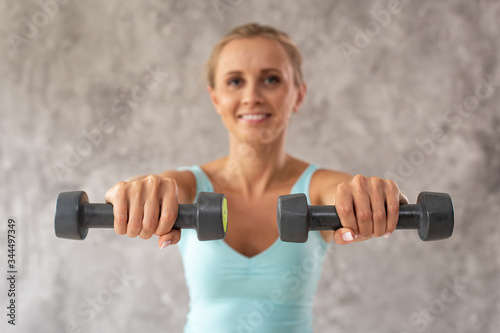 Smiling woman in sport outfit holds two dumbbells in hands. Portrait photo. Selective focus