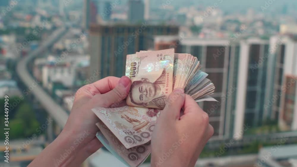 Thai baht bills - counting money on building's rooftop big city Bangkok cityscape