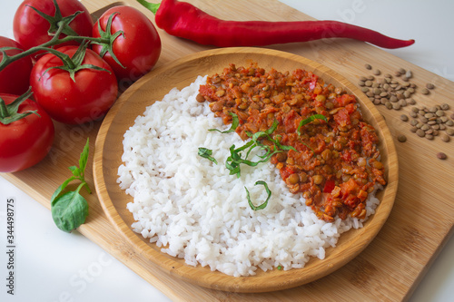 Red lentil ragu dahl with tomatoes, pepper, greens and rice on a wooden plate