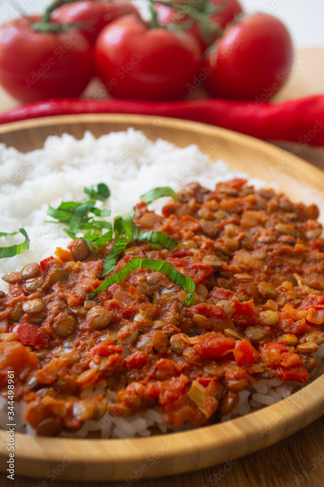 Red lentil ragu dahl with tomatoes, pepper, greens and rice on a wooden plate