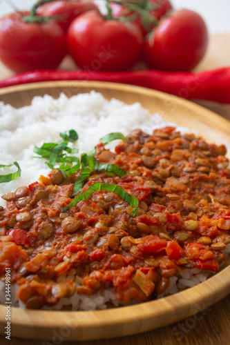 Red lentil ragu dahl with tomatoes, pepper, greens and rice on a wooden plate