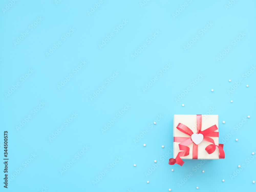 Obraz premium White giftbox with red ribbon and white heart on blue background with beads. Mother day, Valentine day, Wedding, Birthday concept. Greeting or invitation card. Flat lay style with copy space.