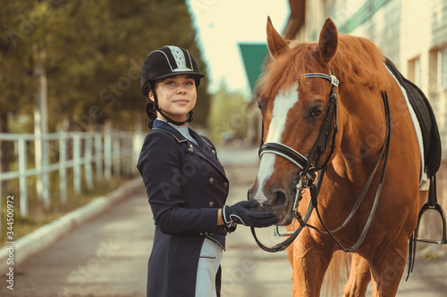 Beautiful professional female jockey standing near horse. woman horse rider is preparing to equitation. girl and horse. equestrian sport concept. dressage horse 