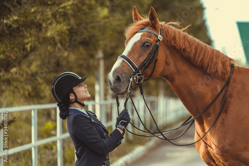 horsewoman jockey in uniform standing with black horse outdoors © matilda553