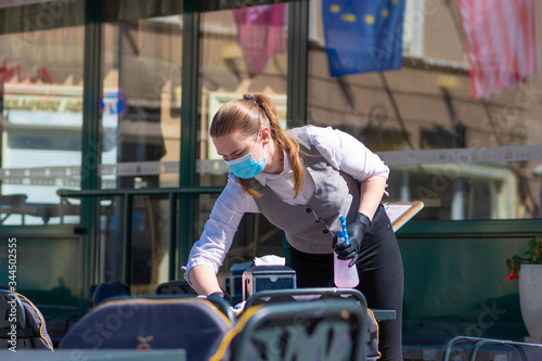 Waitress with a mask disinfects the table of an outdoor bar, café or restaurant, reopen after quarantine restrictions  photo