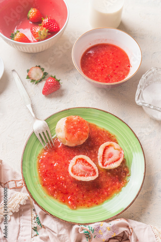 Close up of tasty boiled cottage dumplings stuffed  with fresh strawberries with sweet berries sauce on white kitchen table. Top view. Summer sweet food. Home cooking. Seasonal meal. Knedliki . photo