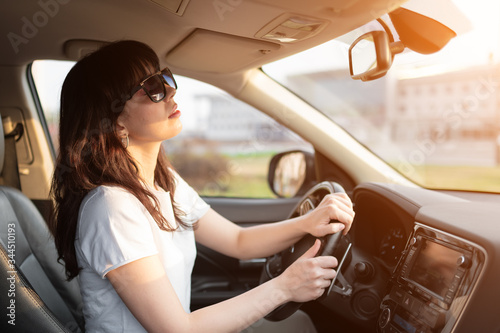 Accurate woman driver looking in inner rearview mirror of her car before drive reverse. Driving rental car in sunny summer day on vacation.
