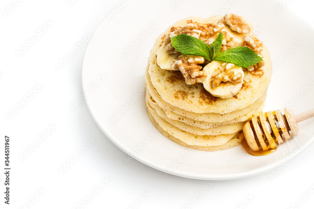Tortitas con rodajas de plátanocon nueces y menta sobre un plato blanco redondo con batuta con miel sobre un fondo blanco aislado. Vista superior. Copy space Tortitas con rodajas de plátanocon nueces y menta sobre un plato blanco redondo con batuta con miel sobre un fondo blanco aislado. Vista superior. Copy space