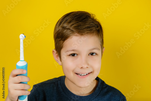 Handsome child brushing teeth with electric toothbrush yellow background.