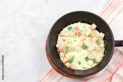Omelette with sausages, green onions, cheese and croutons on frying pan on a light gray background. Top view, flat lay