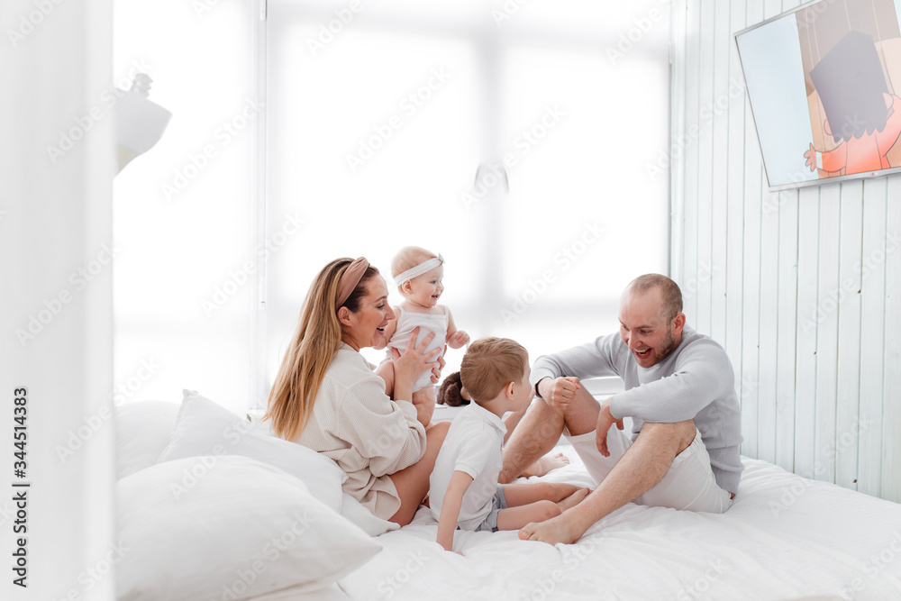 A young happy family with young children lying around, hugging, laughing on the bed at house